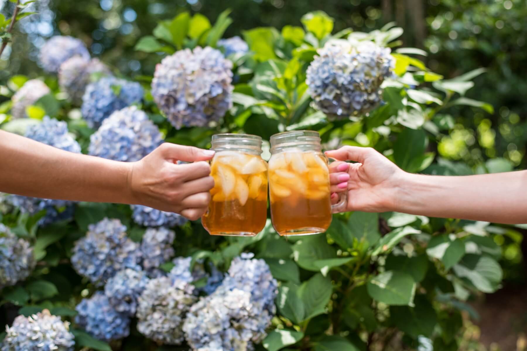 two people holding mason jars of iced tea in a 'cheers' hold