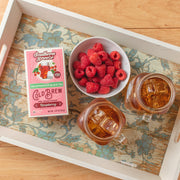 Southern Breeze Decaf Raspberry Sweet Iced Tea pack on a tray with two iced tea jars and raspberries in a bowl