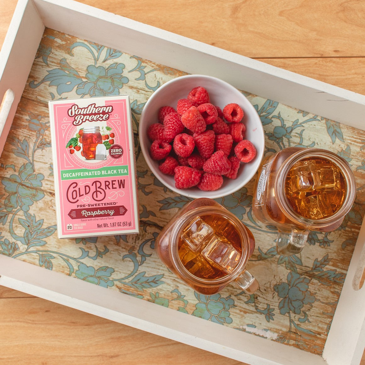 Southern Breeze Decaf Raspberry Sweet Iced Tea pack on a tray with two iced tea jars and raspberries in a bowl