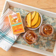 Southern Breeze Decaf Mango Sweet Iced Tea pack on a tray with two iced tea jars and mango slices in a bowl