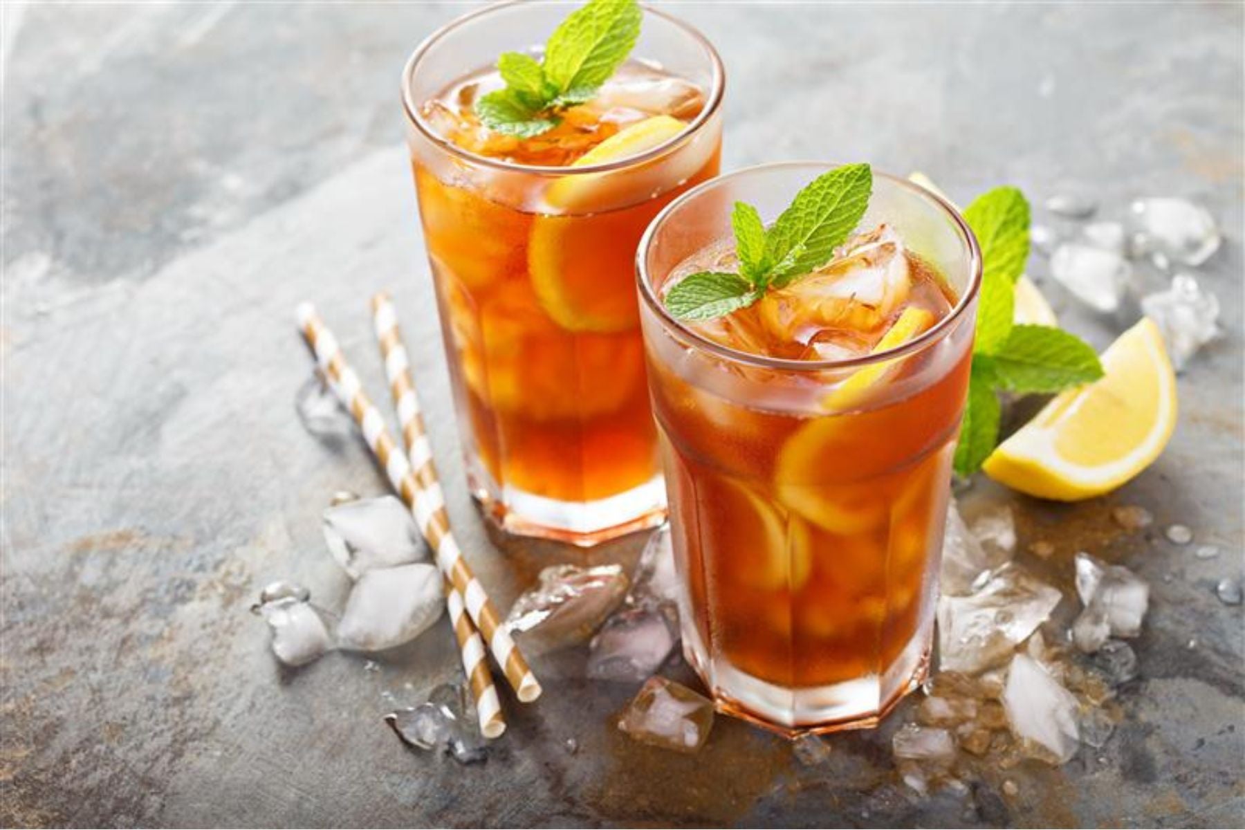 Two glasses of iced tea with lemon and mint surrounded by ice cubes.