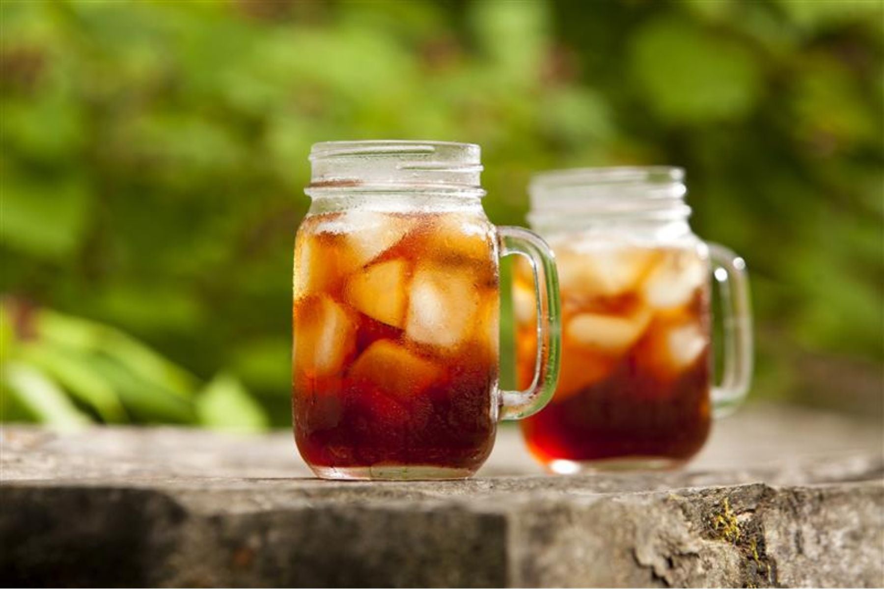 Two mason jars of iced tea with ice.