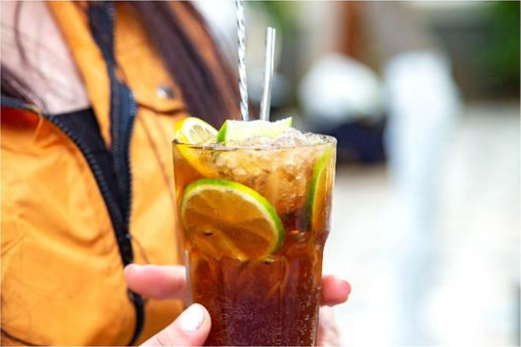 A person holding a glass of Iced tea with lemon wedges in it