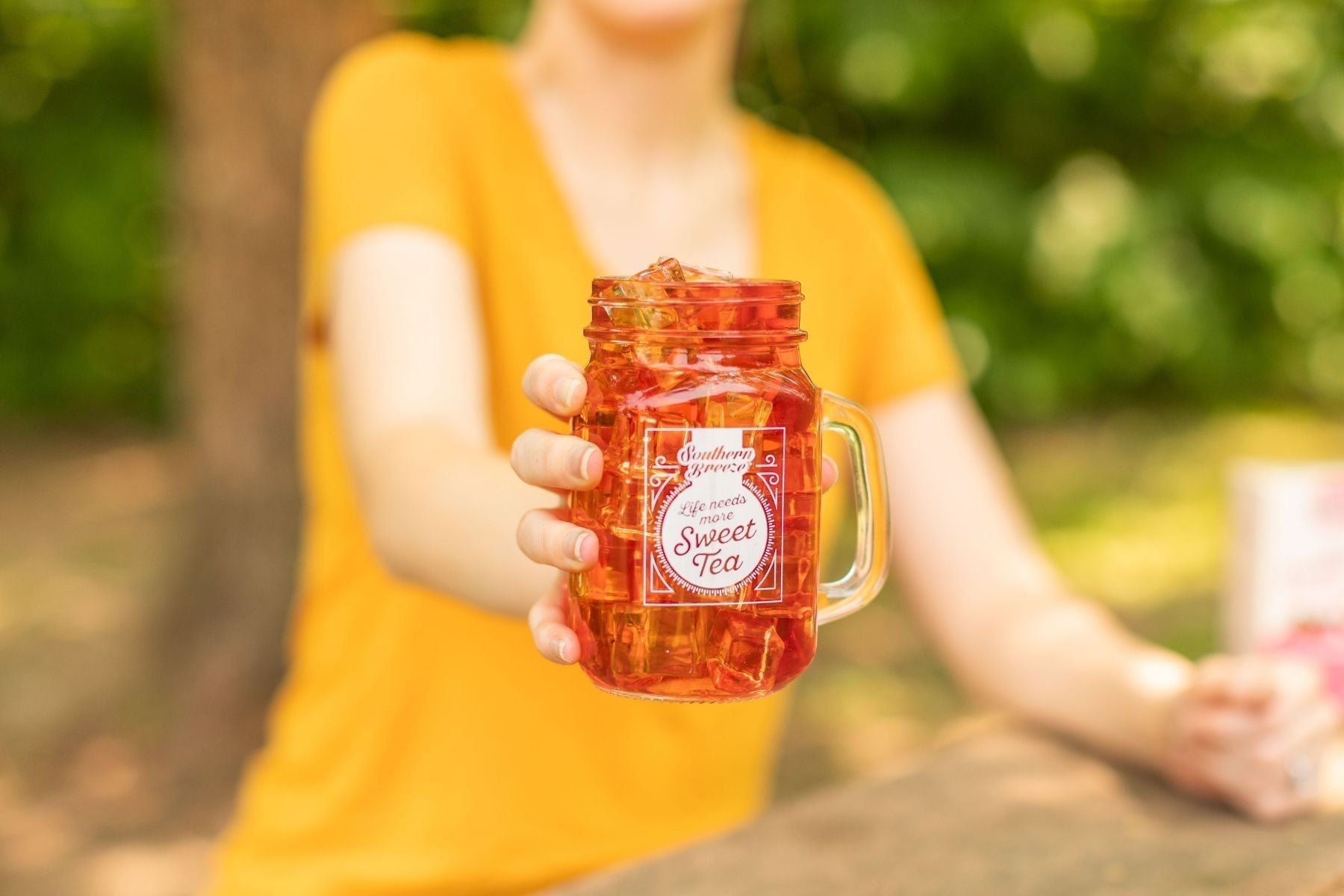 A person holding a mason jar full of iced tea