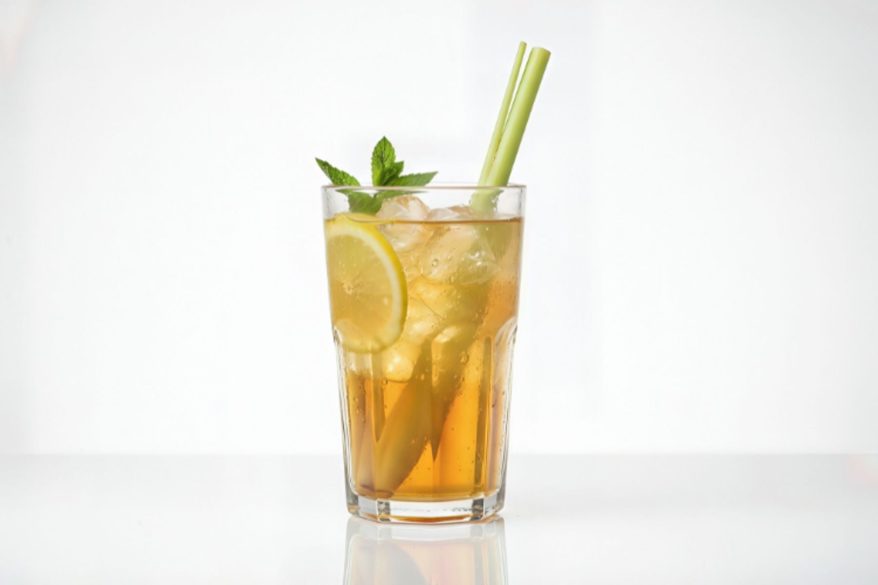 A glass full of Iced Tea with a lemon wedge, mint leaf and straw in it