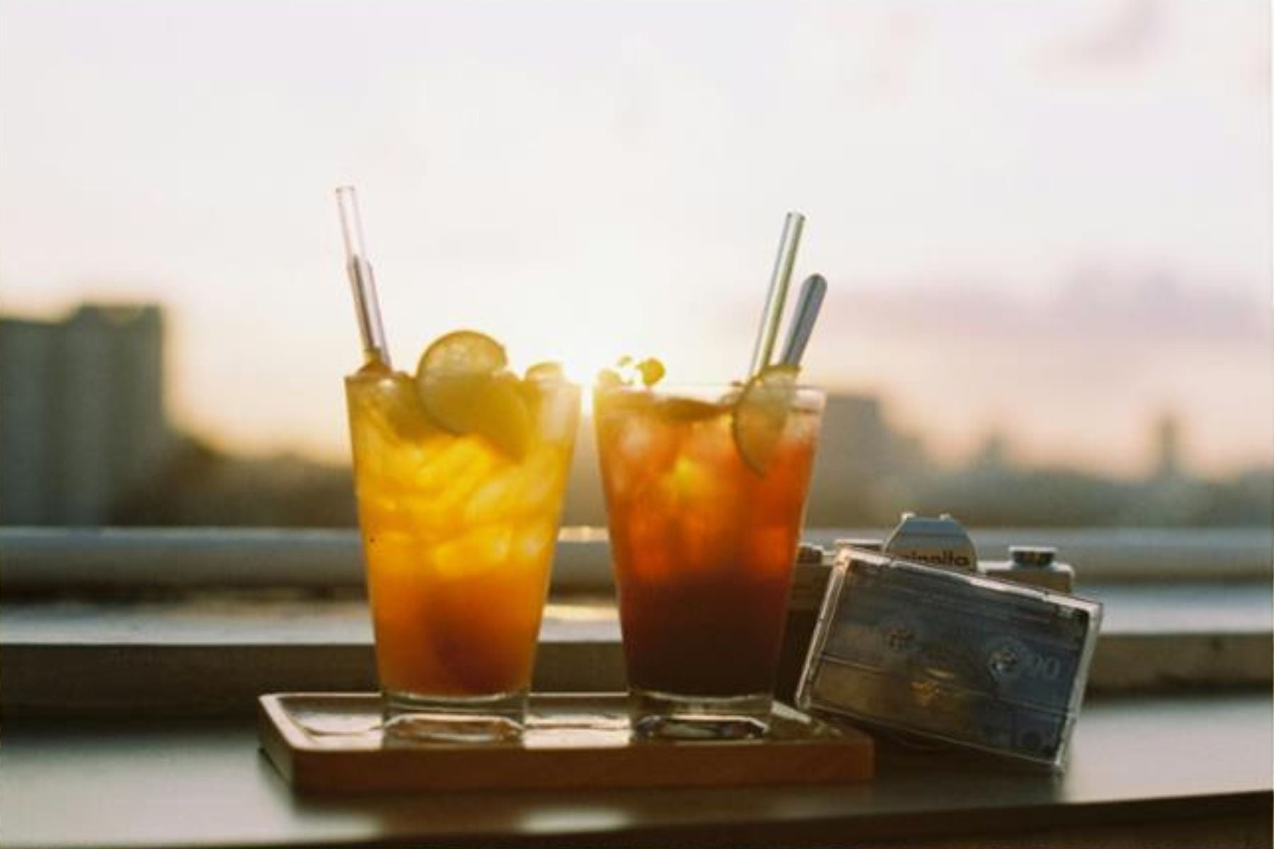 Two glasses of iced tea with lime slices on a tray at sunset with a camera beside them