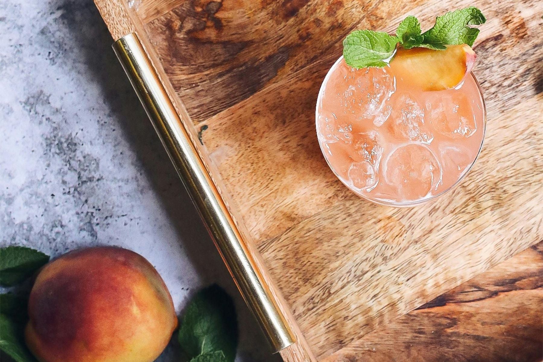 A glass of Peach Tea on a wooden board alongside a peach