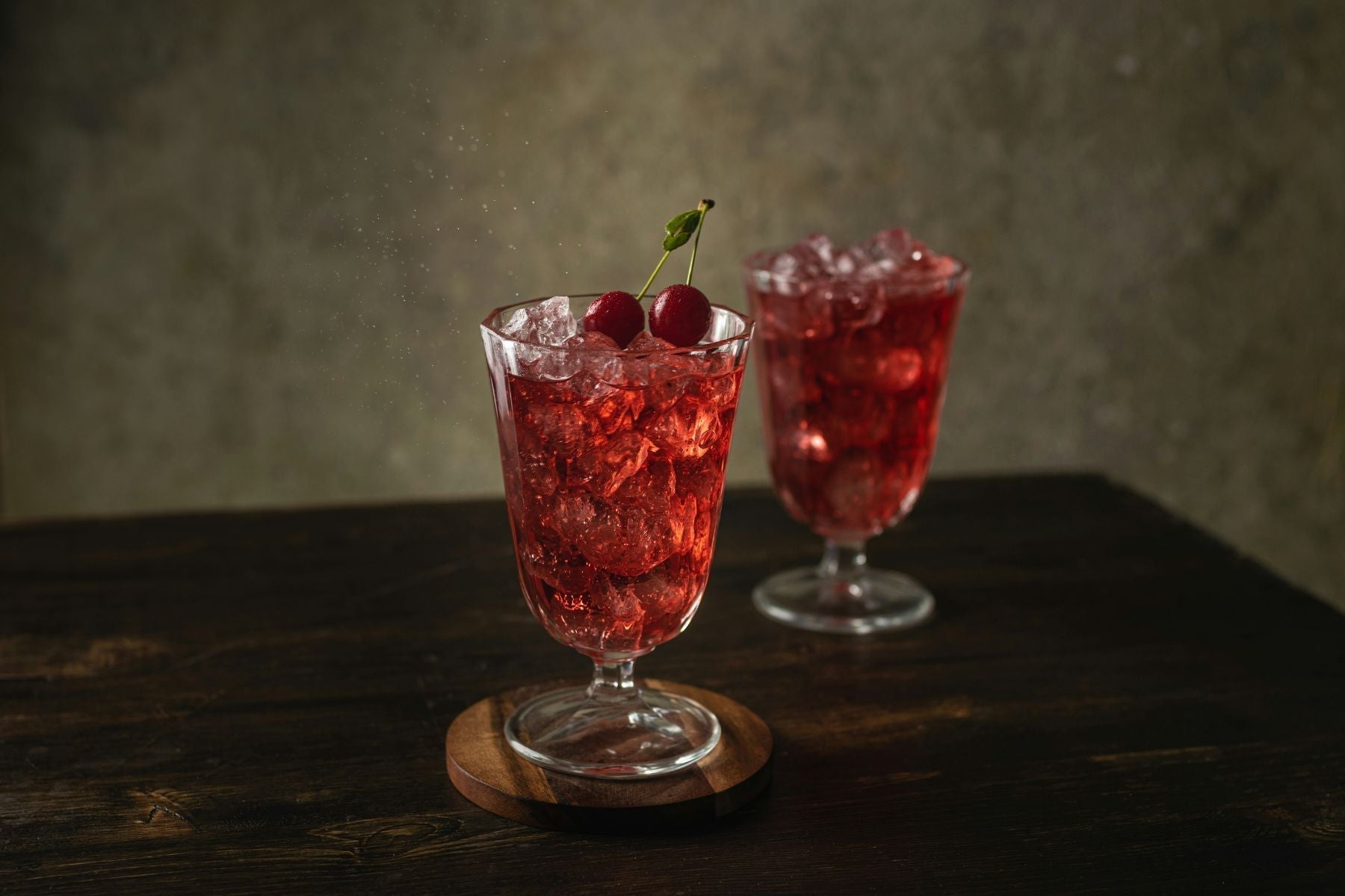 Two glasses of Cherry Amaretto Bliss Mocktail with ice and cherry garnish on a dark wooden surface