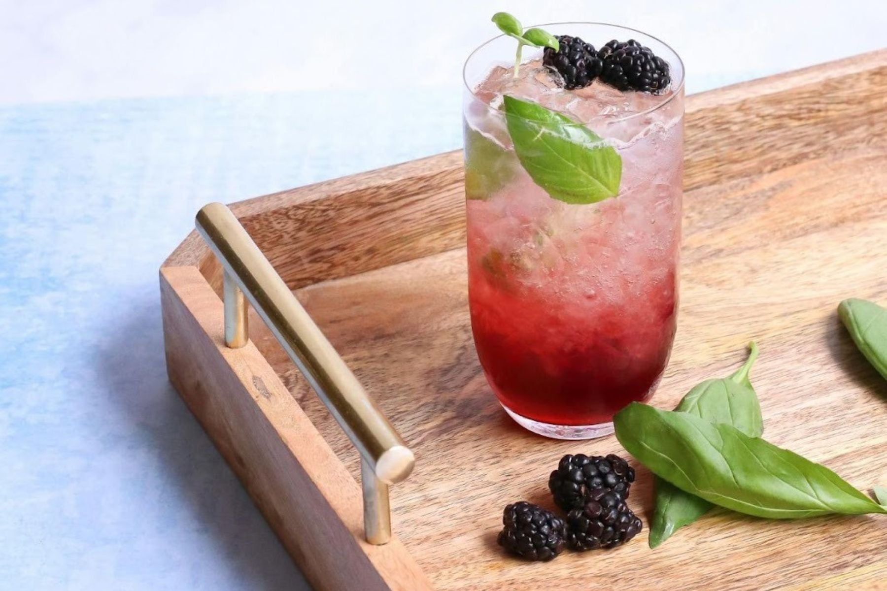 Blackberry Sweet Tea Spritzer with basil garnish and fresh berries served on a wooden tray