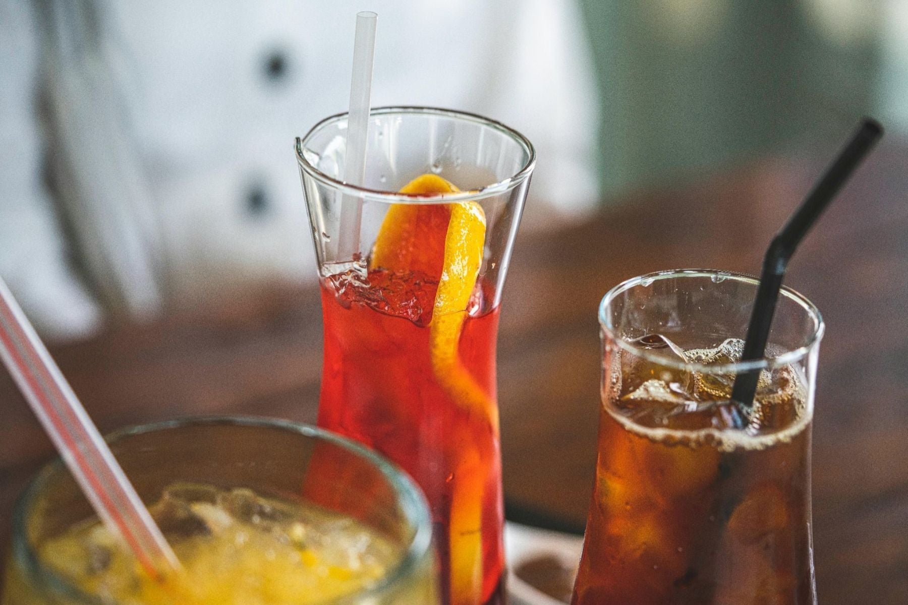 Assorted iced tea drinks in tall glasses, including a red citrus tea with an orange slice and a dark iced tea with a straw