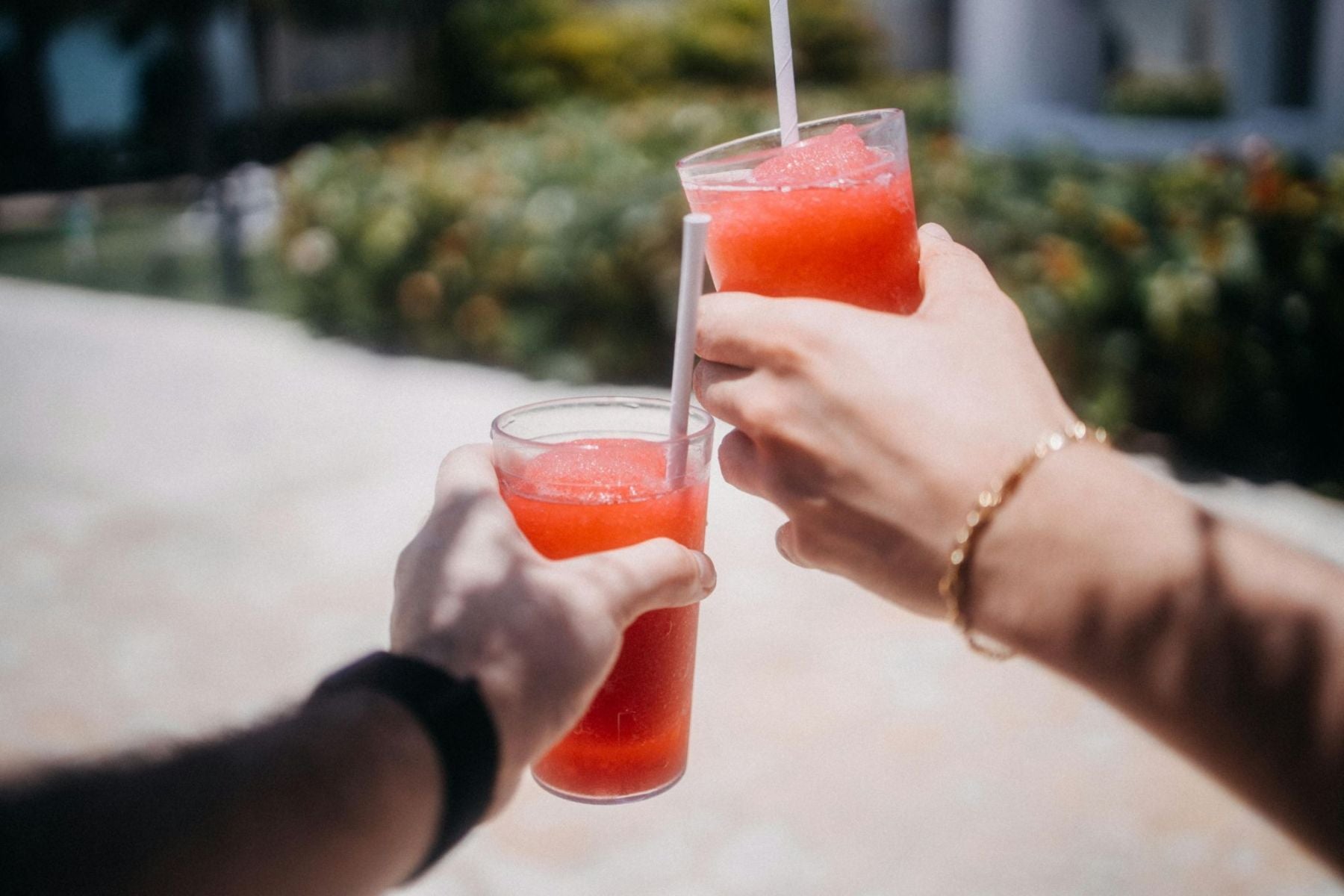 Two people clinking glasses of bright red watermelon slushies outdoors