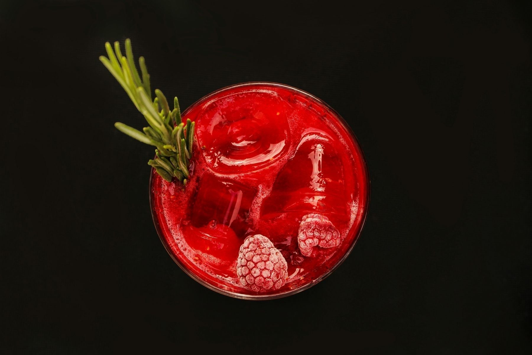 Top view of bright Raspberry Sweet Tea Mocktail with raspberries and rosemary garnish on a black background