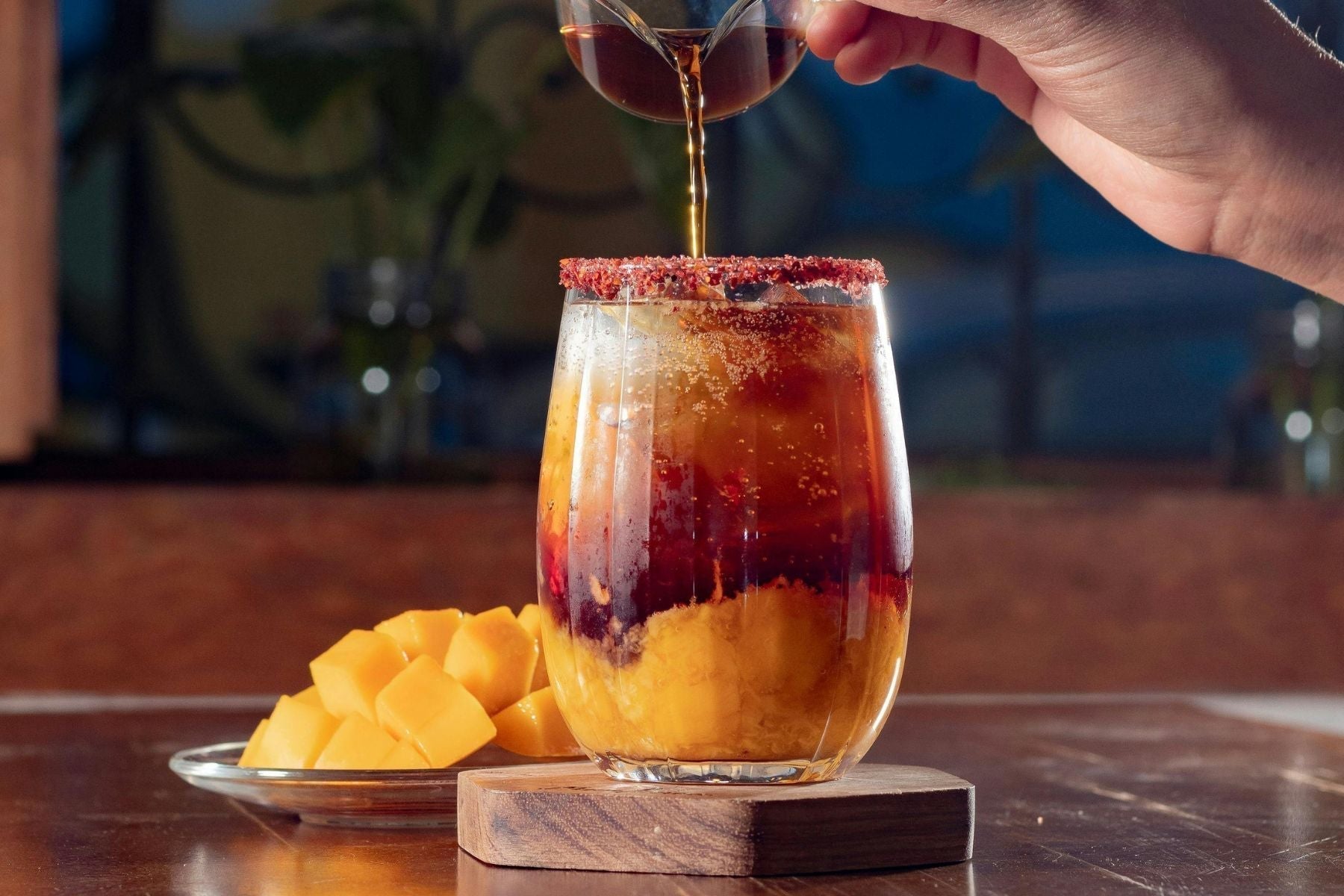 Mango iced tea being poured over ice with layered fruit and tea in a glass