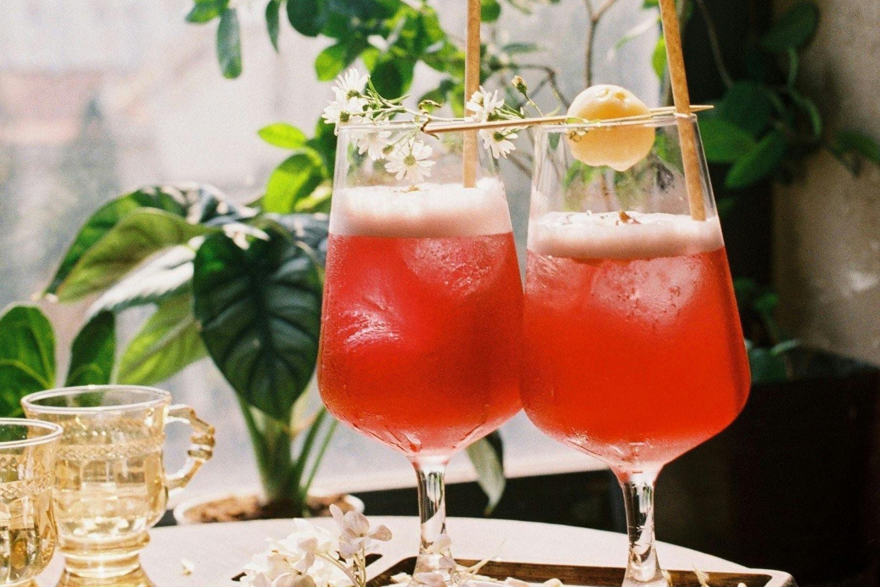 Cherry Rose Sweet Tea Spritz in stemmed glasses with foam and floral garnish in a sunlit setting