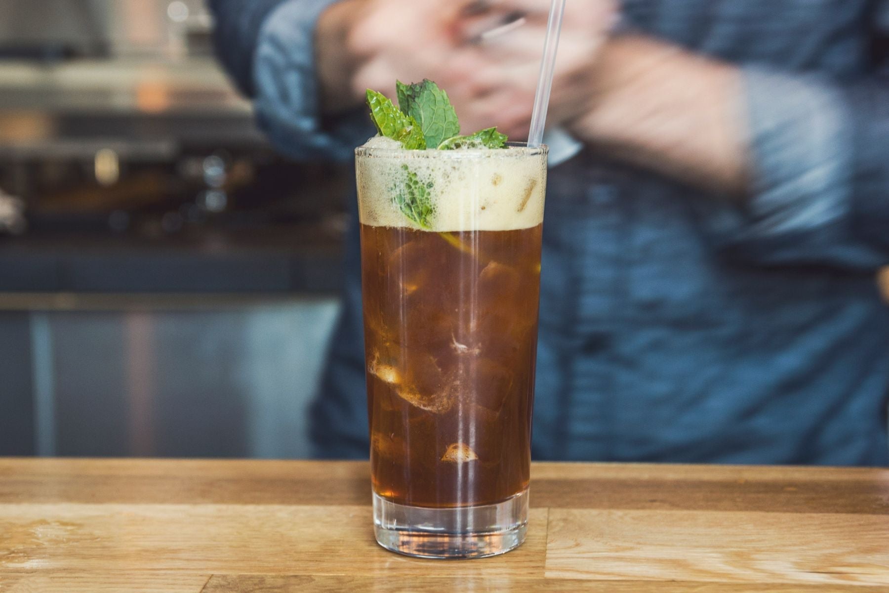 Tall glass of Basil Lime Sweet Tea Mocktail on a café counter with a bartender in the background