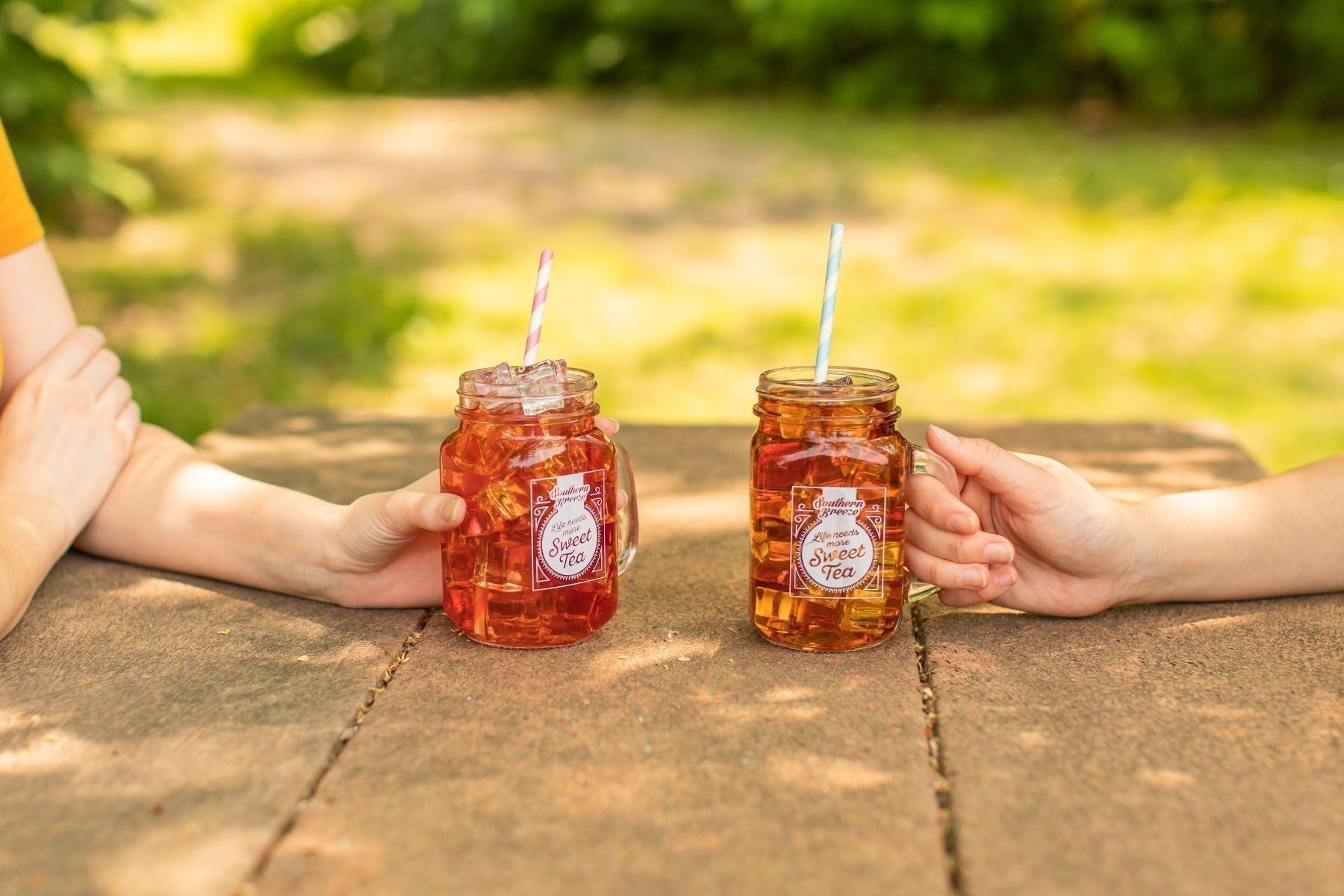 Two mason jars of Southern Breeze iced sweet tea with straws held on a picnic table