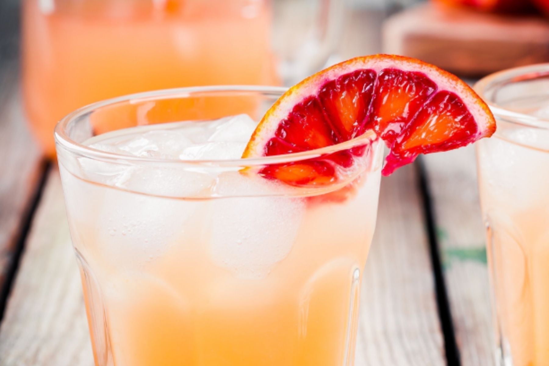 Iced Tequila Sunrise cocktail with a blood orange slice garnish on a rustic wooden table.