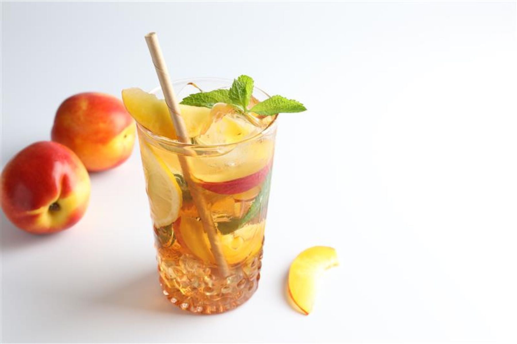 Iced tea with peach, lemon, and mint on a white background.