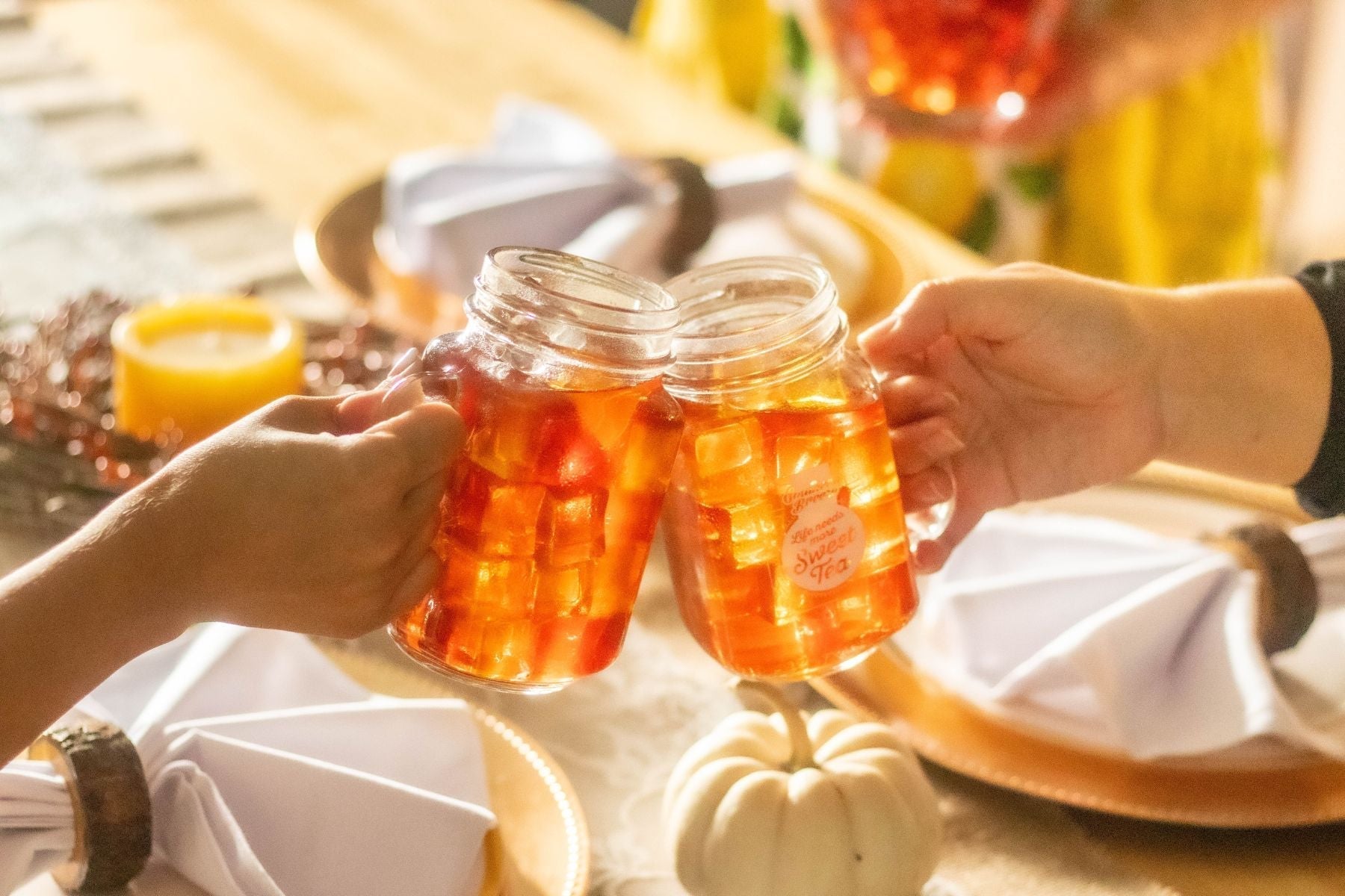 Two hands toasting with mason jars of iced tea over a table.