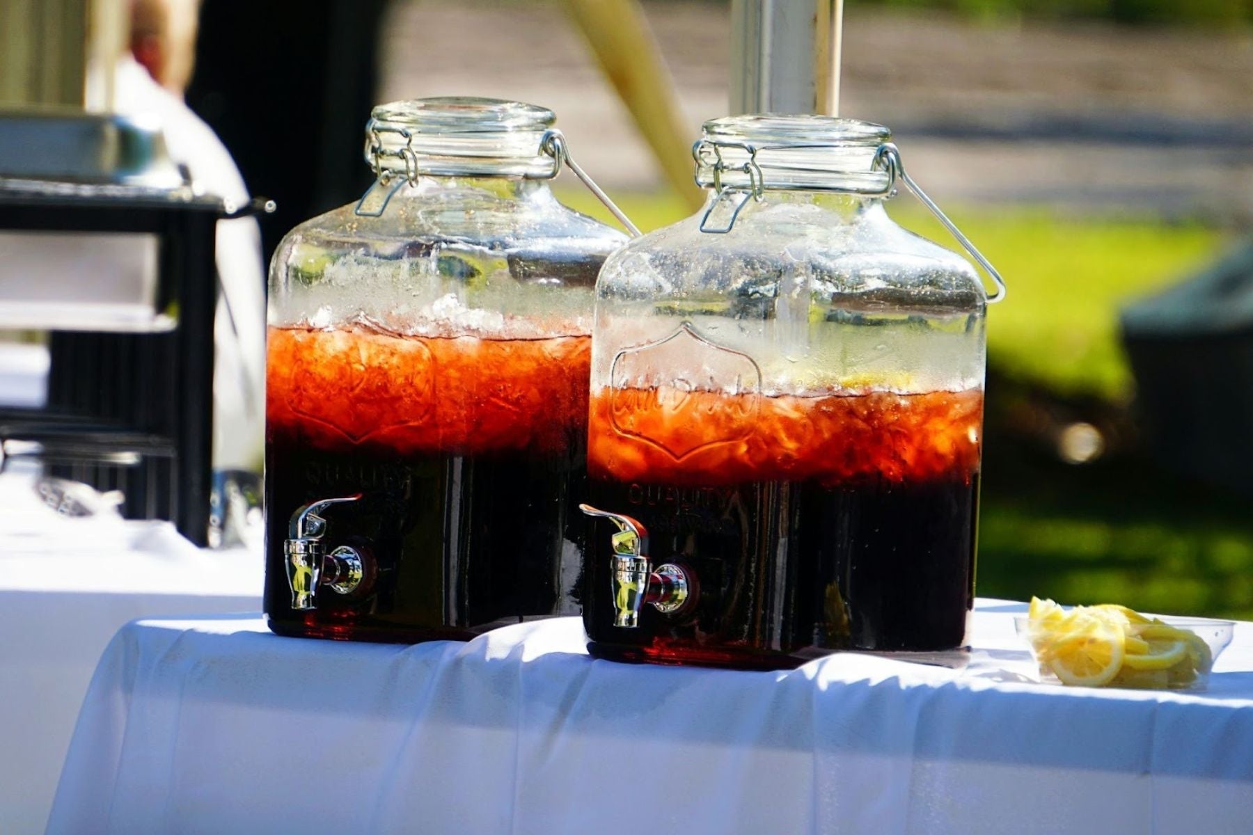 Two large iced tea dispensers on a white outdoor table.