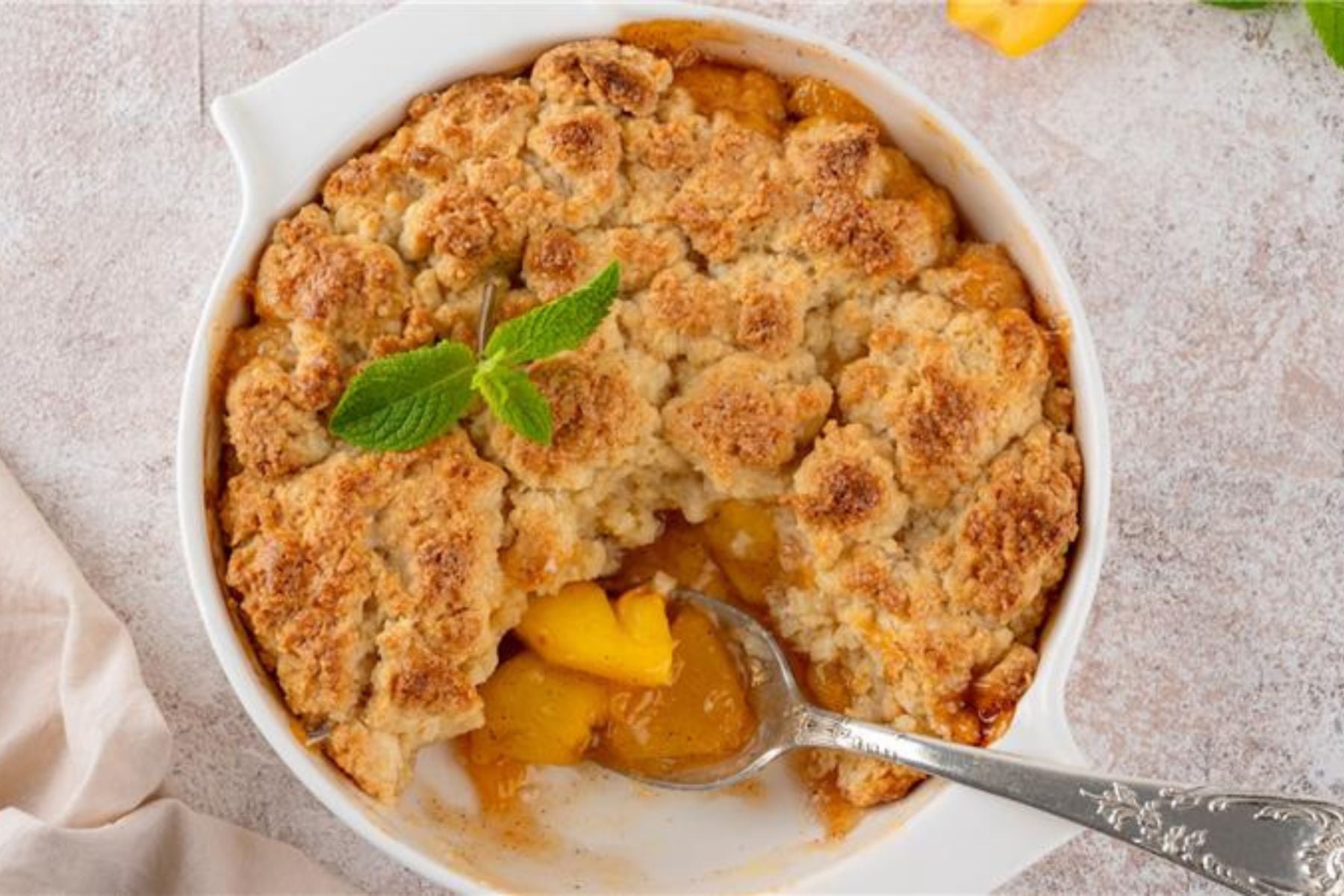 Peach cobbler in a white baking dish with a spoon scooping out a serving.
