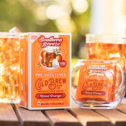 Southern Breeze pre-sweetened cold brew tea packaging and glass on a wooden surface with blurred greenery in the background.