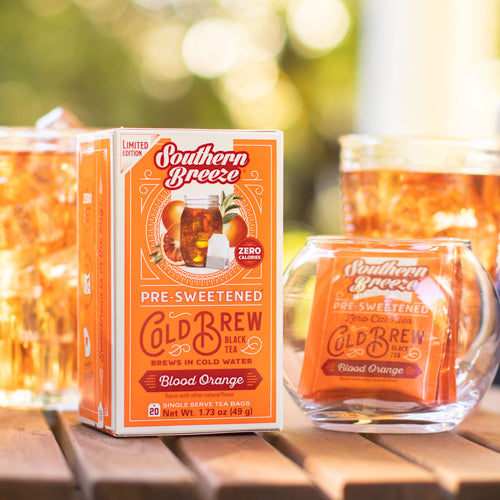 Southern Breeze pre-sweetened cold brew tea packaging and glass on a wooden surface with blurred greenery in the background.