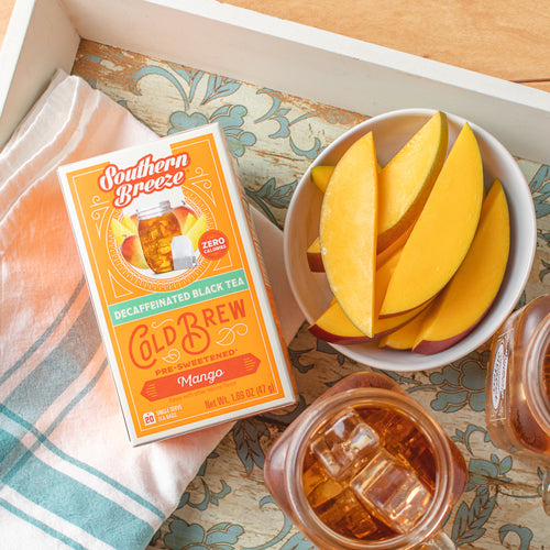 Southern Breeze Cold Brew Mango tea package with a bowl of mango slices and a glass of iced tea on a patterned cloth.