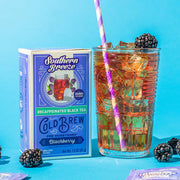 Glass of iced tea with a straw next to a box of Southern Breeze Cold Brew Blackberry tea on a blue background