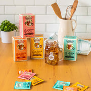 The boxes are in different flavor colors: Original (teal), Peach (orange), Raspberry (pink), and Half & Half (yellow). Next to it is a mason jar of sweet iced tea that says "Life Needs More Sweet Tea", all on a kitchen counter