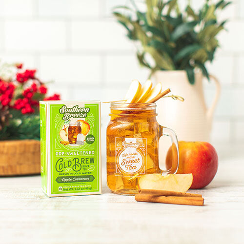 Jar of sweet tea with a box of Southern Breeze tea on a table with apples and cinnamon sticks.