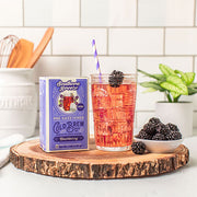 Southern Breeze pre-sweetened cold brew blackberry tea package with a glass of iced tea and blackberries on a wooden board.