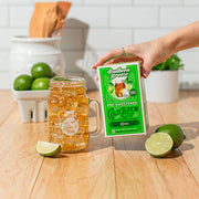 Hand holding a box of Southern Breeze pre-sweetened cold brew Lime tea with a glass mug of tea on a wooden surface and limes