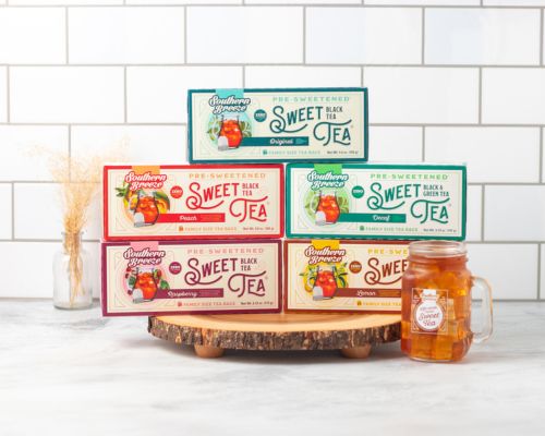 Assorted boxes of Southern Sweet Tea on a wooden stand with a mug in front against a white tiled wall.