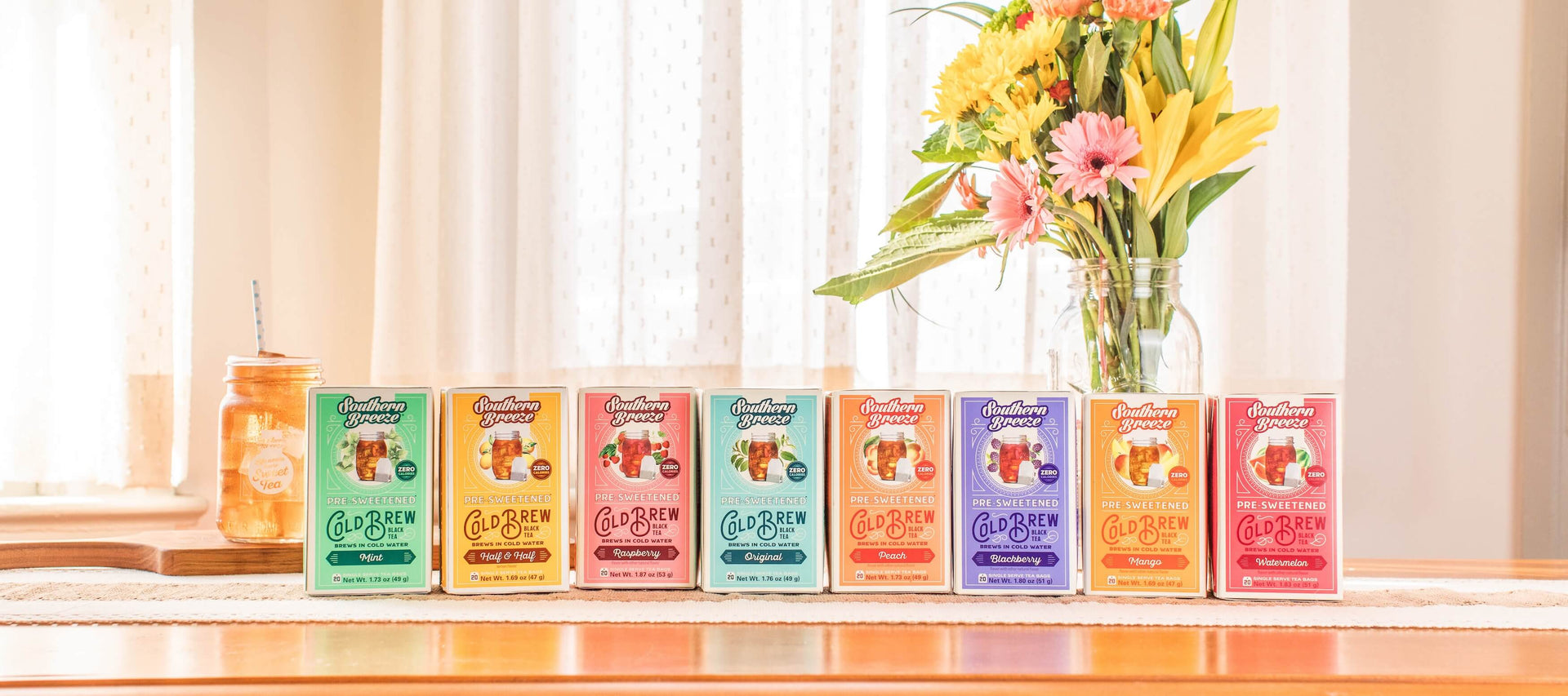 cold brew tea flavors lined up in a row in bright sunny room with flowers in mason jar vase in background. 